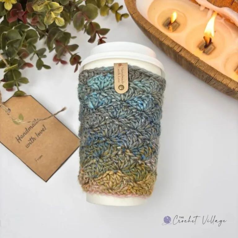 Blossom Cup Cozy crochet patterns in blue, gold, and grey variegated shell stitch, one flat and one on a coffee cup with a copper hook