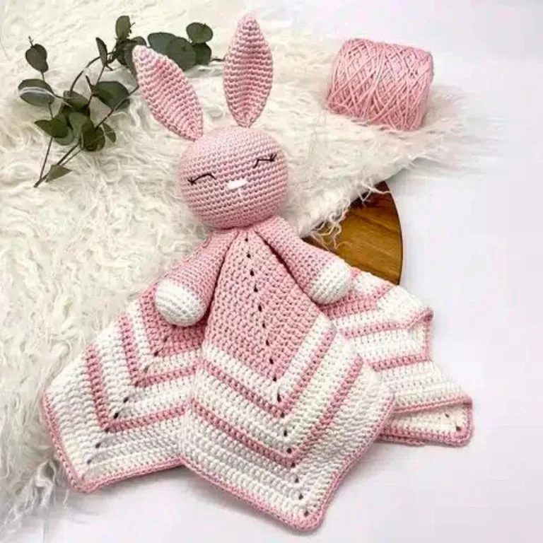 A lovely crochet lovey blanket laid out on a carpet, accompanied by a yarn ball, showcasing a cozy and handmade touch.