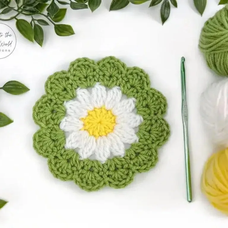 A crochet coaster in the shape of a flower, with a crochet hook and yarn balls nearby.