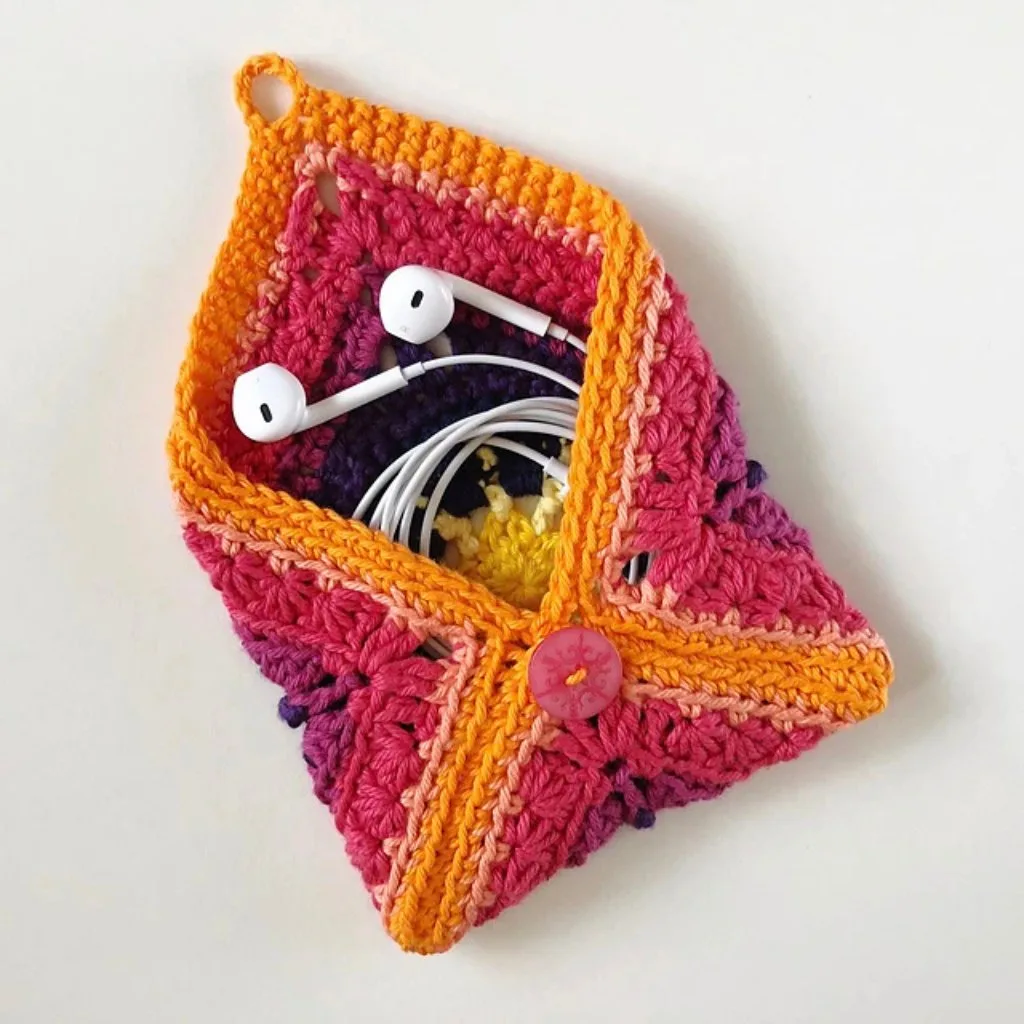 Earbuds neatly tucked inside a granny square crochet pouch made from colorful yarn scraps,