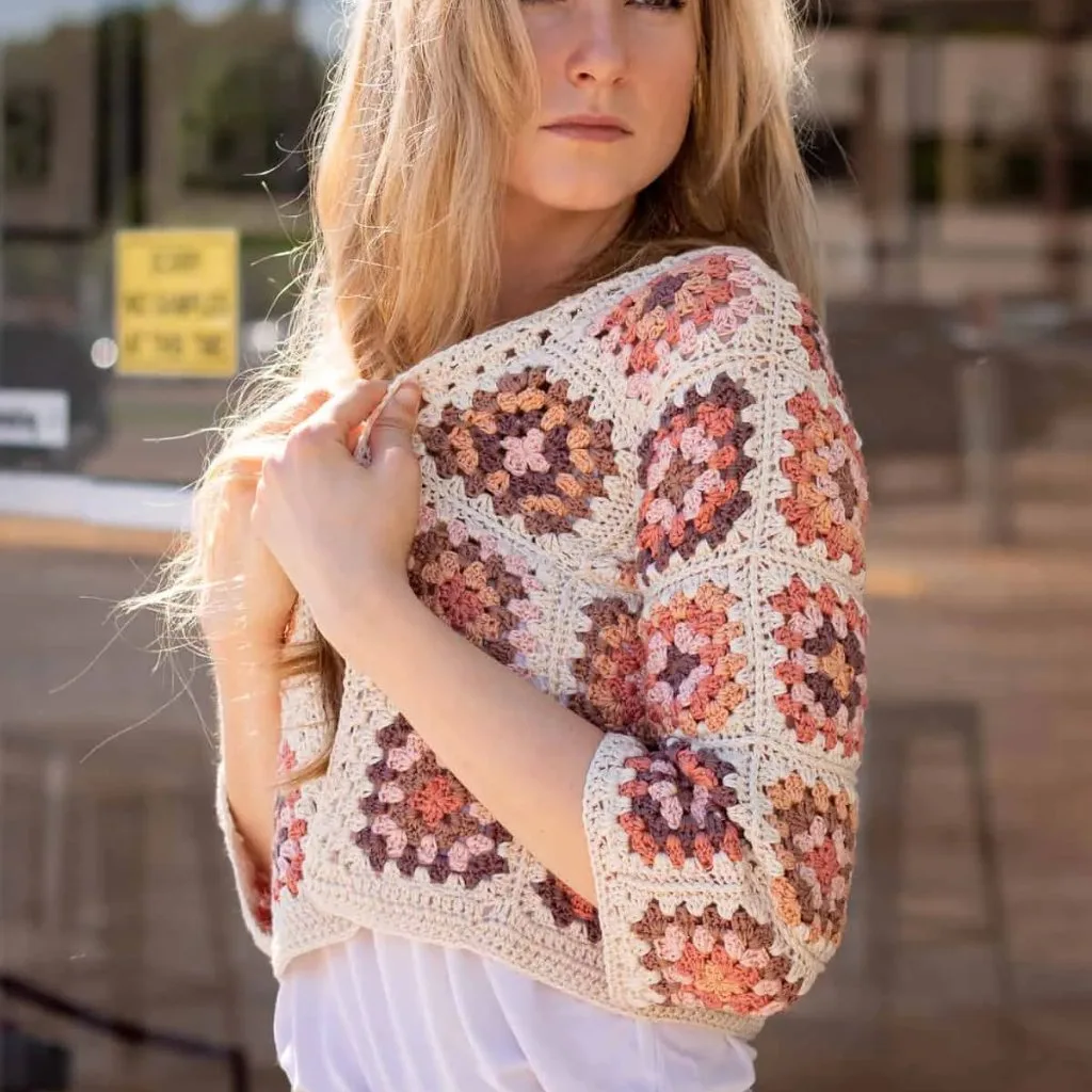 A young woman wearing a crochet cropped granny square cardigan made with yarn scraps