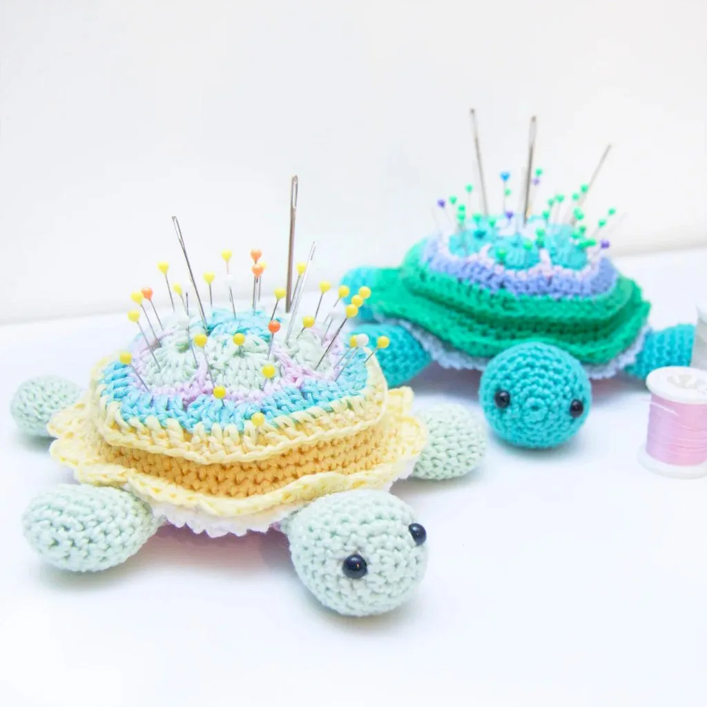 Two crochet pincushions in the shape of turtles, each holding sewing needles and pins.