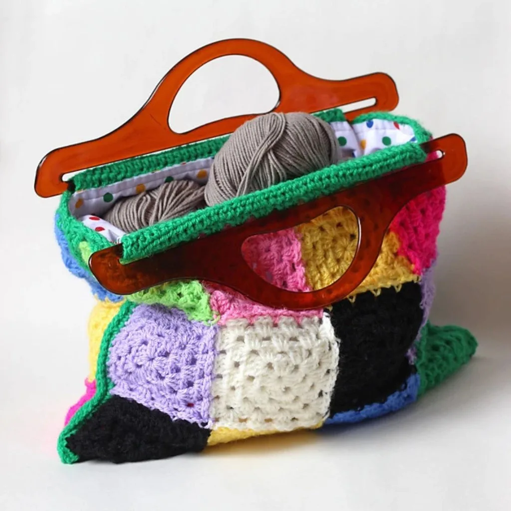 A Crocheted granny square bag with plastic handles filled with yarn.
