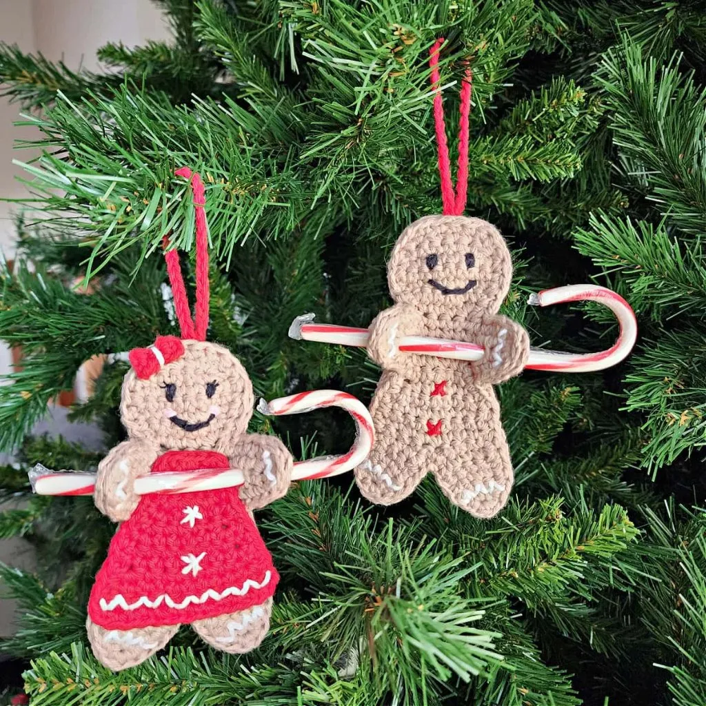 Two Crochet gingerbread men holding candy canes, hanging on a christmas tree.