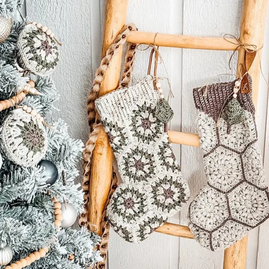 Two crochet granny square Christmas stockings hanging on a wooden ladder by a Christmas tree.