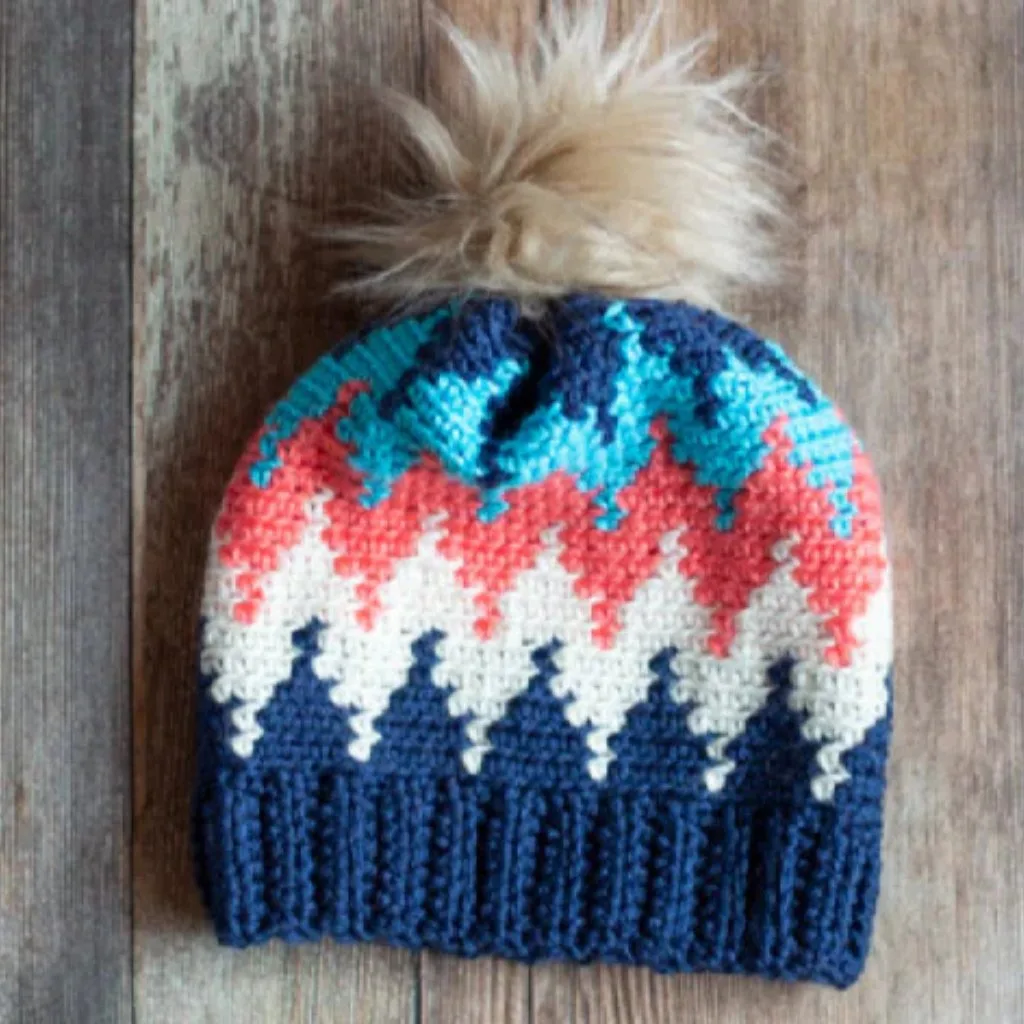 Colorful crochet beanie with a pom pom on a wooden surface.