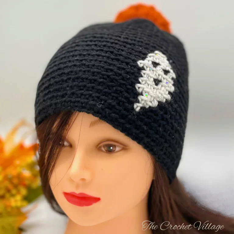 Black crochet beanie featuring a white ghost print, topped with a bright orange pom pom