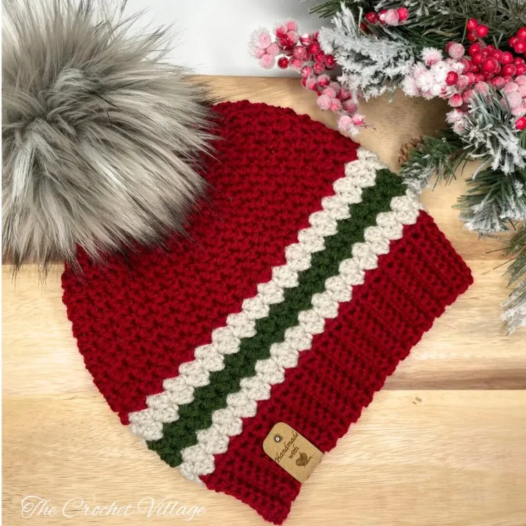 A crochet festive striped Christmas hat with a large pom-pom, displayed with Christmas picks.