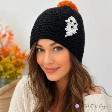 Black crochet beanie featuring a white ghost print, topped with a bright orange pom pom