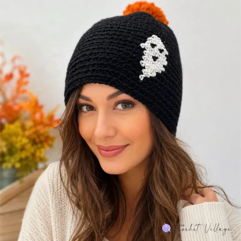 Black crochet beanie featuring a white ghost print, topped with a bright orange pom pom
