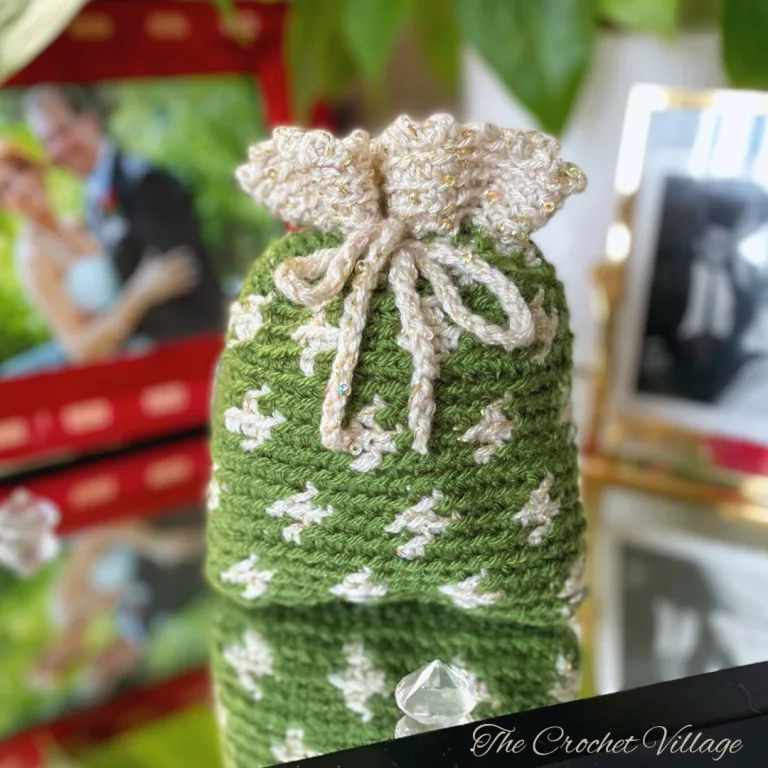 .A small festive crochet gift bag in green and beige with gold accents, perfect for holiday gifting.