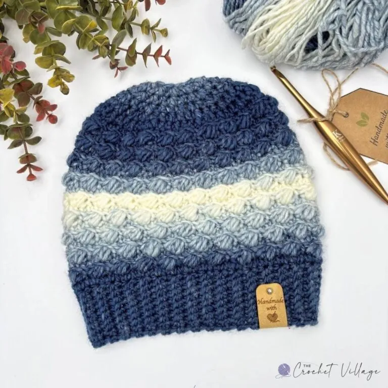 Beginner crochet hat laid flat in blue ombré yarn, with the ribbed brim and puff stitch rows clearly visible