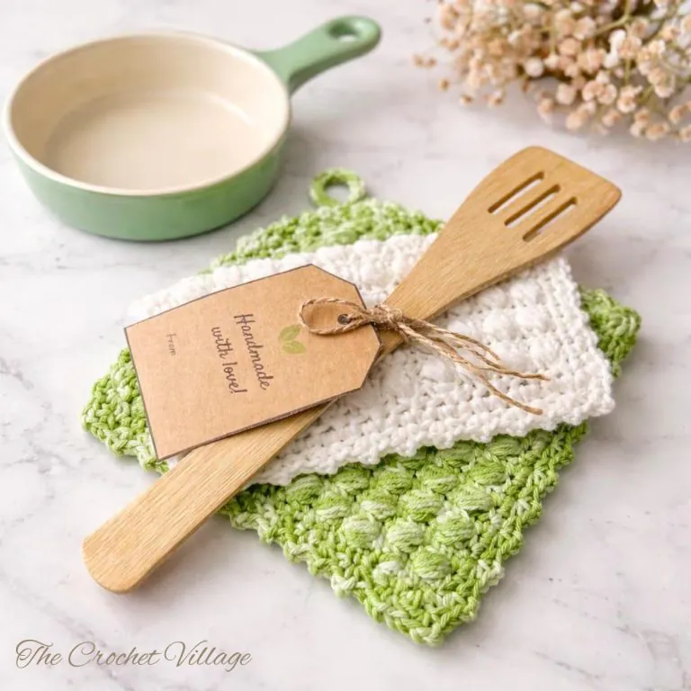 Two folded crochet potholders with a wooden spoon and handmade with love label on a kitchen counter