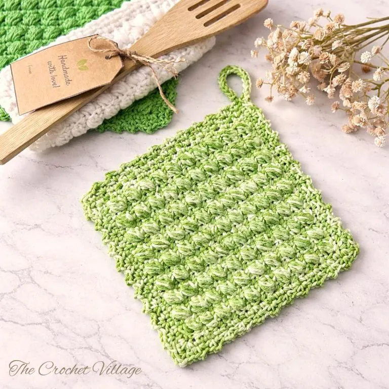 Lucia's textured crochet potholder laying flat on a kitchen surface showing pretty stitch texture, decorative border, and practical hanging loop