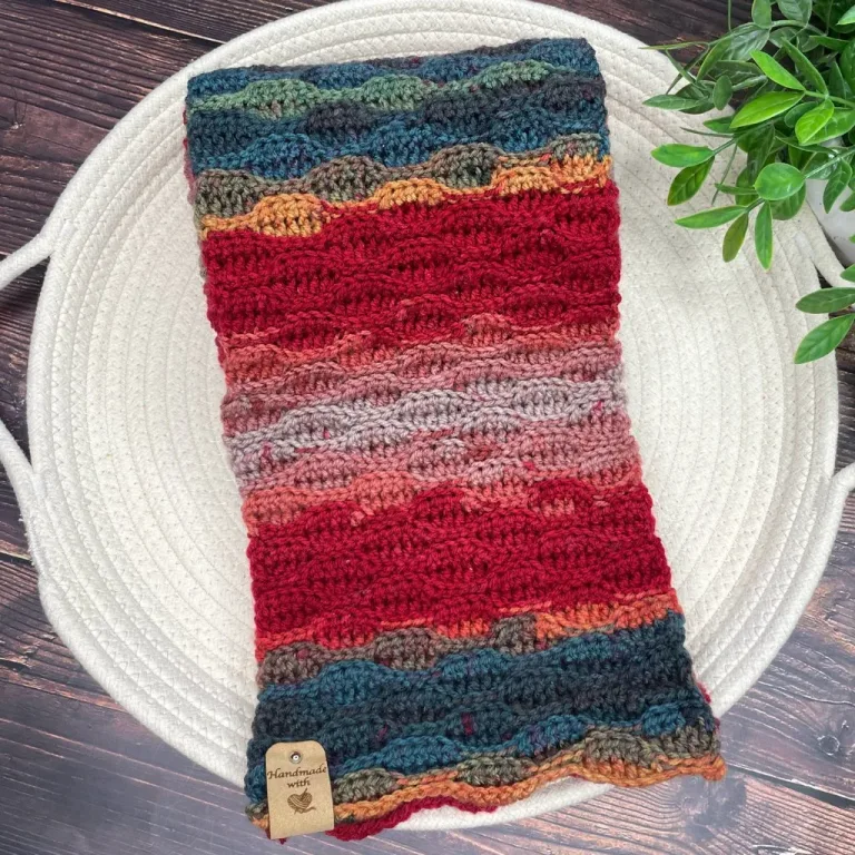 A vibrant, lightweight boho scarf neatly folded beside a lush green plant.