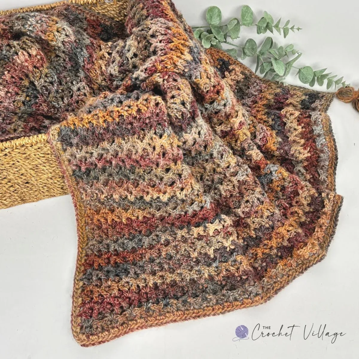 Waffle V stitch crochet blanket folded over a woven basket in fall yarn colors