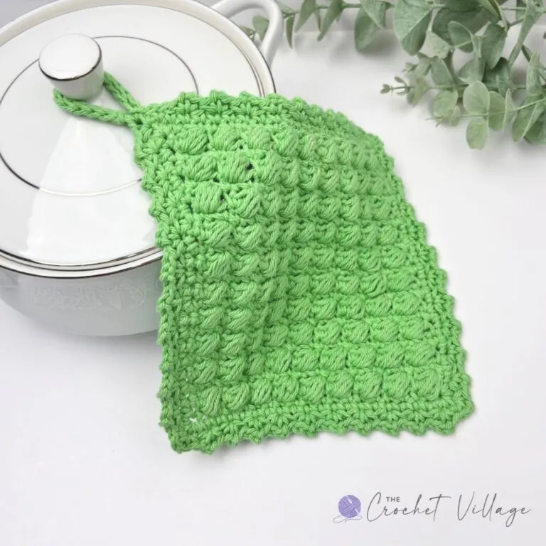 Two folded crochet potholders with a wooden spoon and handmade with love label on a kitchen counter