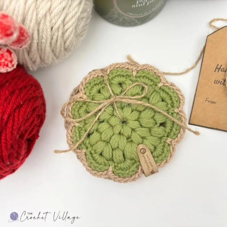 Green crochet Noel coaster with puff stitch texture and tan-border, next to a coffee mug and bag of coffee beans