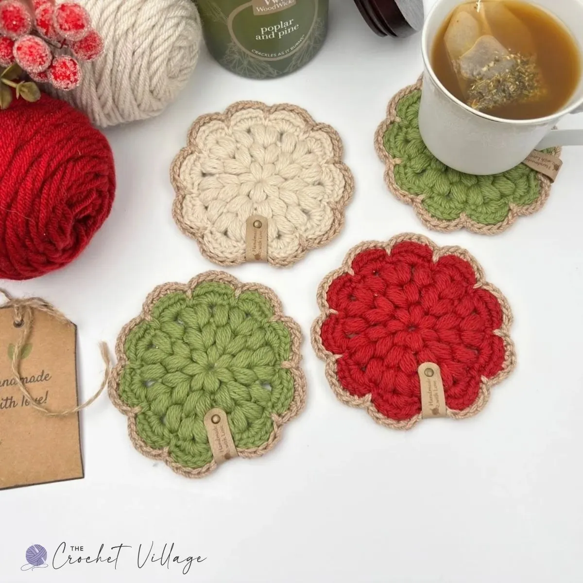 Set of festive crochet Noel coasters in red, cream, and green, showcasing textured puff stitches and handmade tags