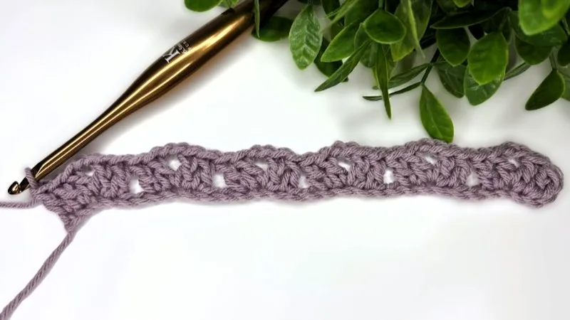 Close-up of a crochet piece with a crochet hook resting beside it.