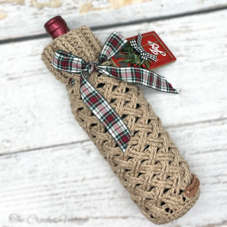 A wine bottle wrapped in a festive crochet Celtic weave stitch cozy, decorated with a Christmas tag for the perfect holiday gift.
