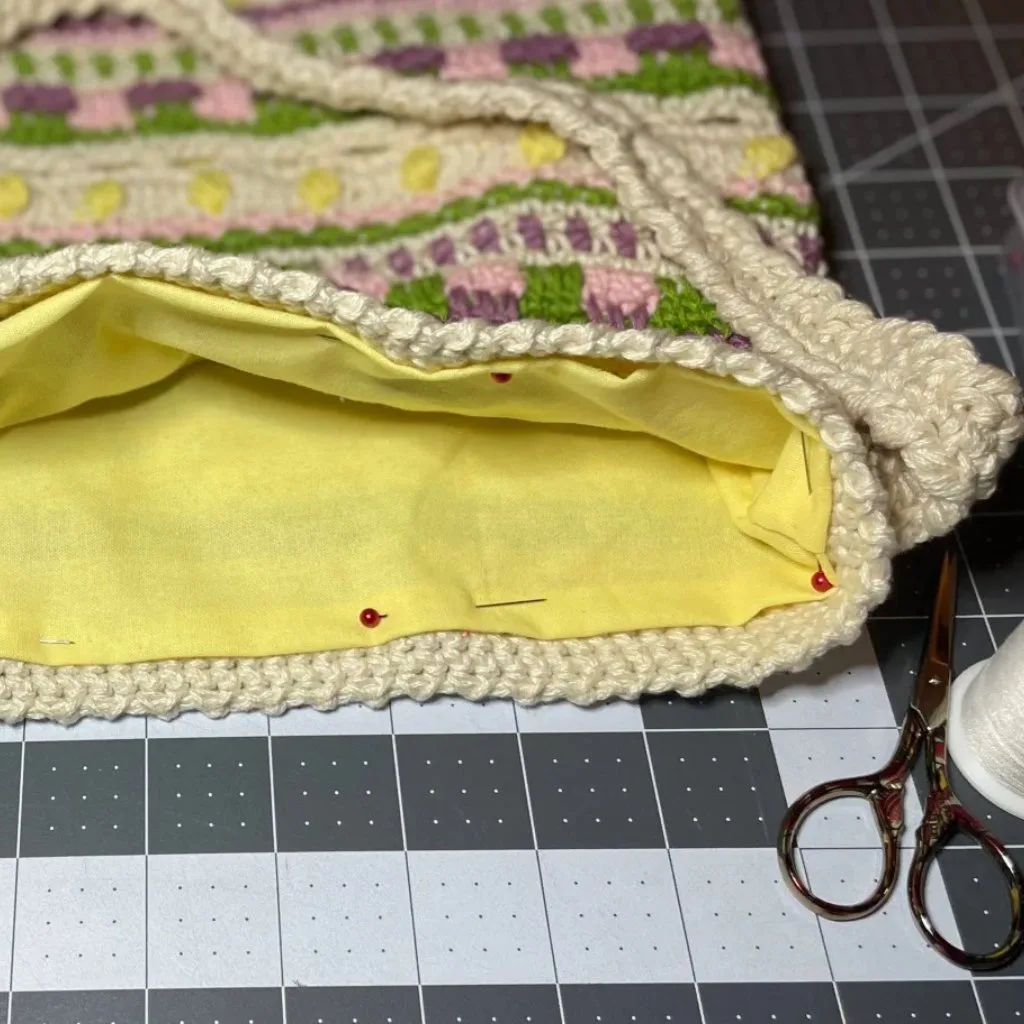 A close-up of the inside of a crochet bag with the lining fabric pinned in place, ready to be sewn.