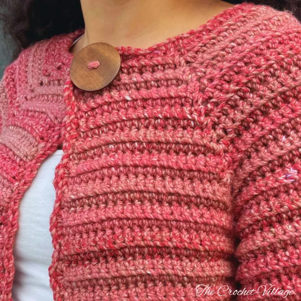 Close-up of the closure of a crochet cardigan featuring a large wooden button, adding a rustic touch to the design.