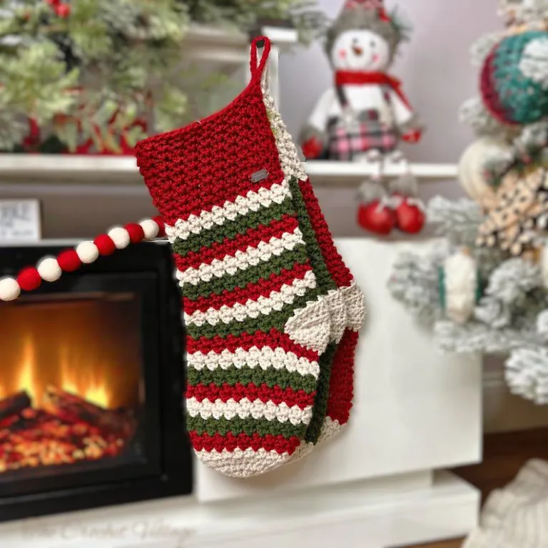 Classic crochet Christmas stockings in solid color and stripes hanging from a fireplace mantel with holiday decorations