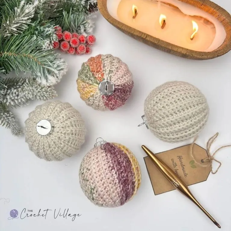 Four crochet Christmas bauble covers in cream and soft variegated pink, green, and gold yarn, with silver buttons and a handmade gift tag