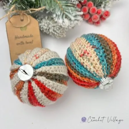 Two crochet Christmas bauble covers one in variegated yarn and one in a solicd color yarn beside a gold crochet hook and a handmade gift tag