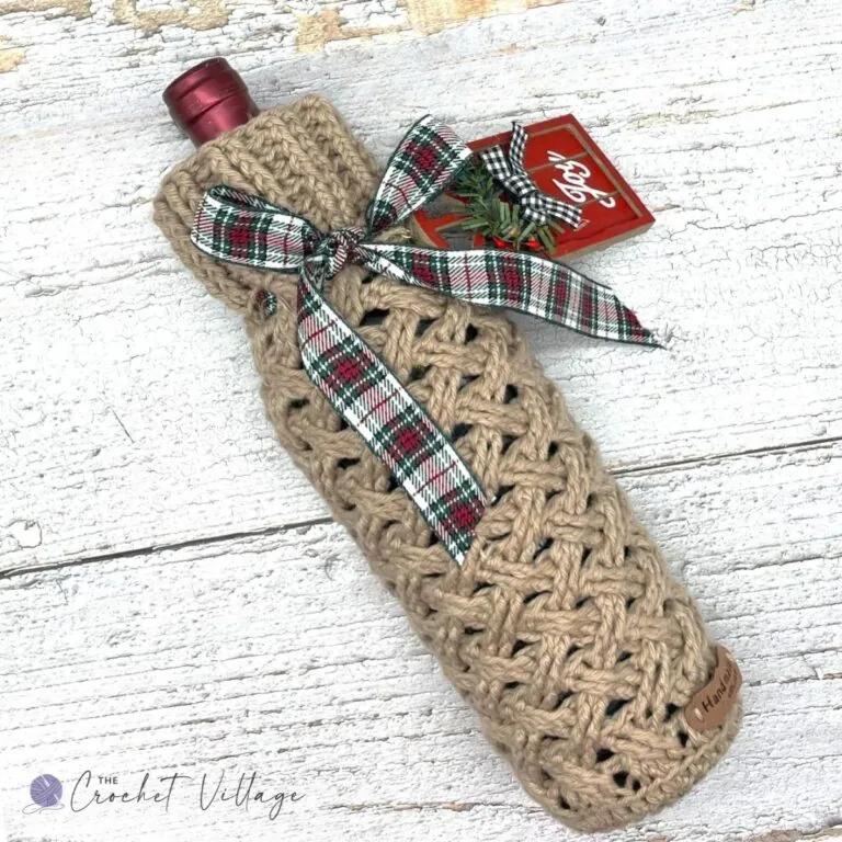Tan crochet wine bottle cozy with Celtic Weave stitch, tied with a plaid Christmas ribbon and gift tag
