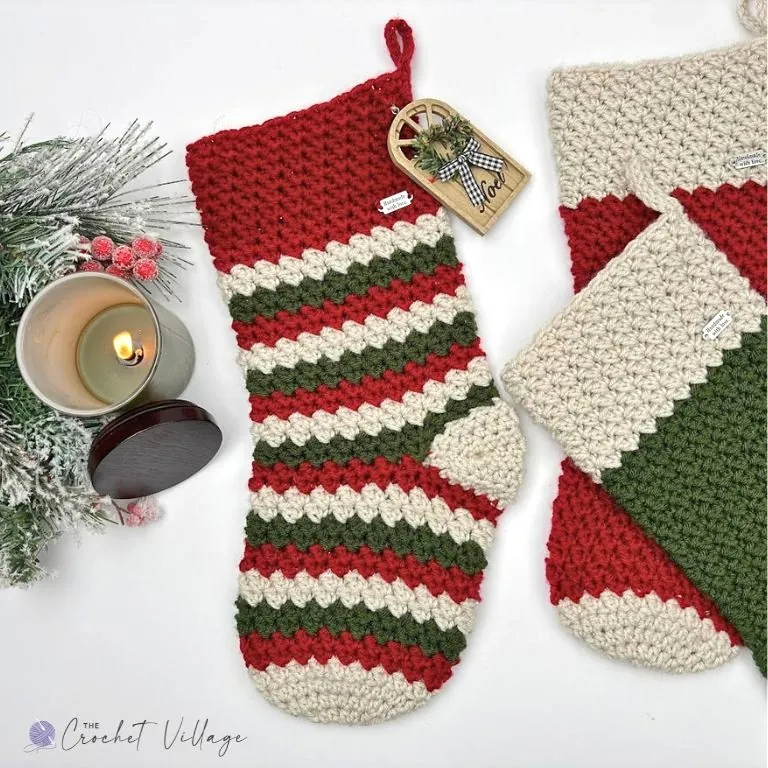 Striped crochet Christmas stocking in red, green and cream with a cream heel and toe, styled with a candle and frosted pine