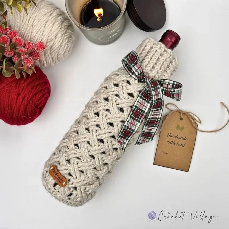 A wine bottle wrapped in a festive crochet Celtic weave stitch cover, decorated with a Christmas tag for the perfect holiday gift.