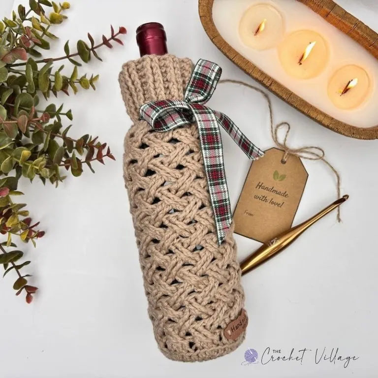 Tan crochet wine bottle cozy with Celtic Weave stitch, tied with a plaid Christmas ribbon and gift tag