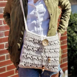 A person carrying a crochet crossbody bag featuring a beautiful shell stitch, with a wooden button and beads.