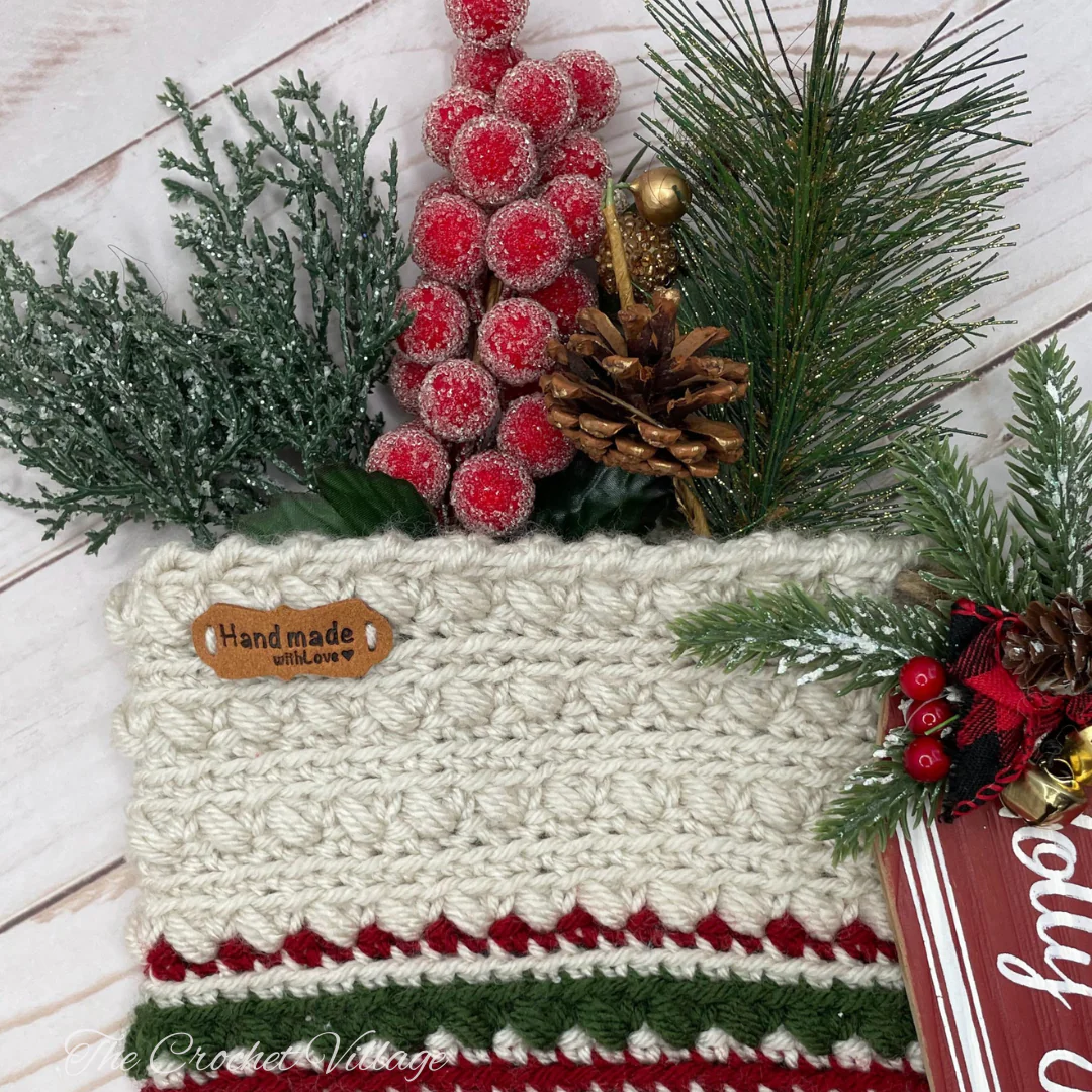 A crochet piece with a "Handmade with Love" tag, adorned with festive Christmas picks.