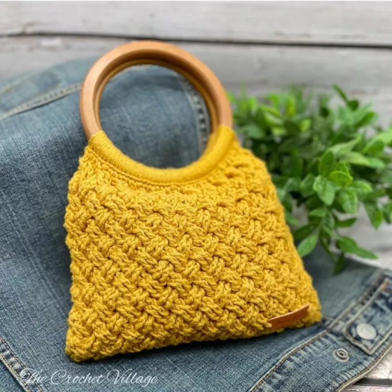 A crochet handbag with wooden handles draped over a jean jacket, highlighting its unique design and texture.