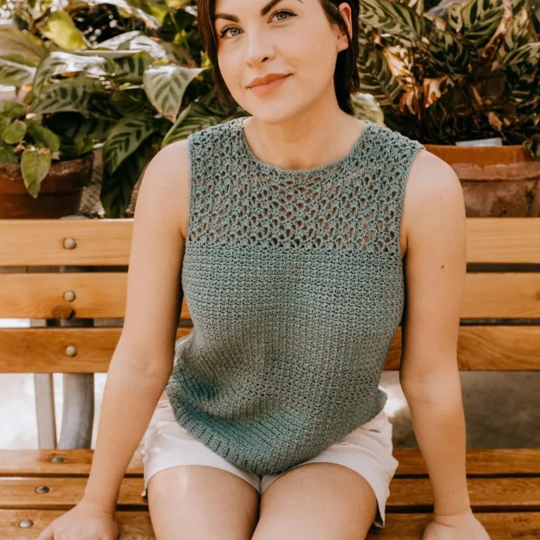 A woman sitting on a bench, wearing a lacy crochet summer top, enjoying a sunny day.