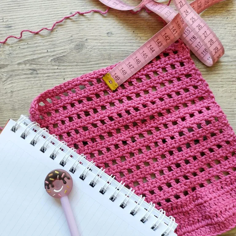 A notebook on a crochet piece with a measuring tape, ready for gauge swatching.