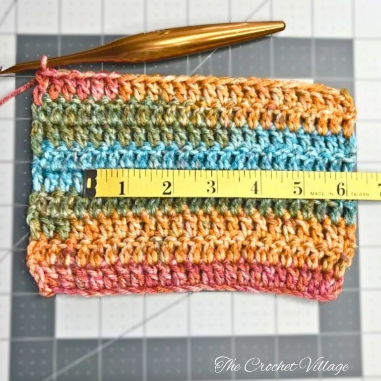 A measuring tape placed horizontally on a crochet square, measuring how many stitches are in the swatch.