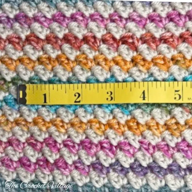 A measuring tape placed on top of a crochet swatch, indicating the number of stitches.