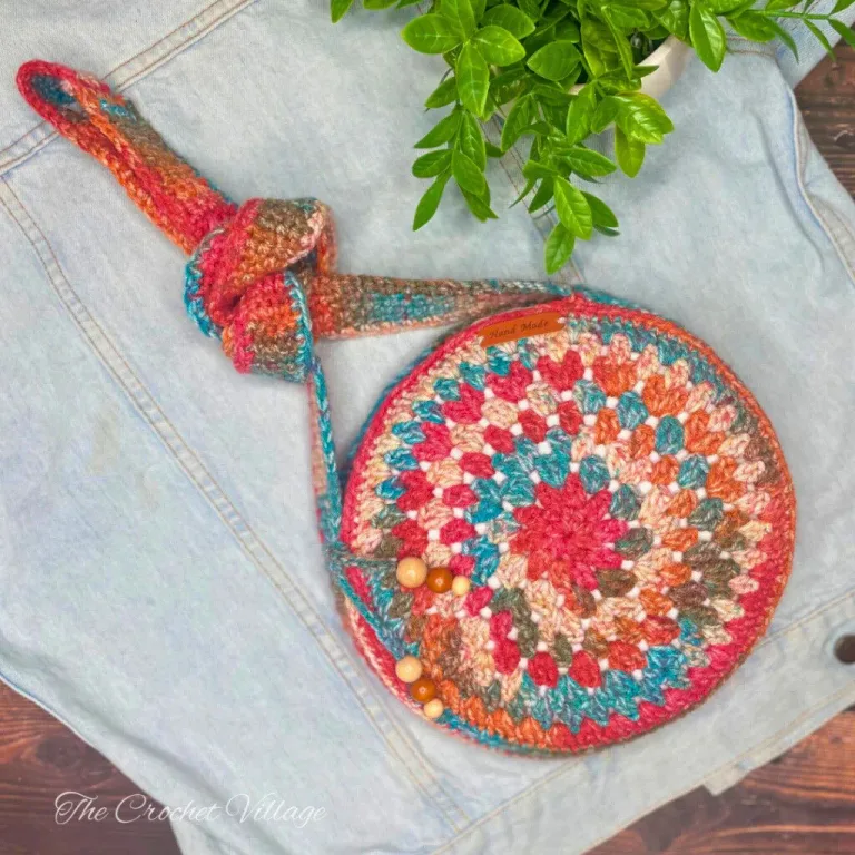 Crochet round bag in boho style displayed on a denim jacket with a plant in the background.