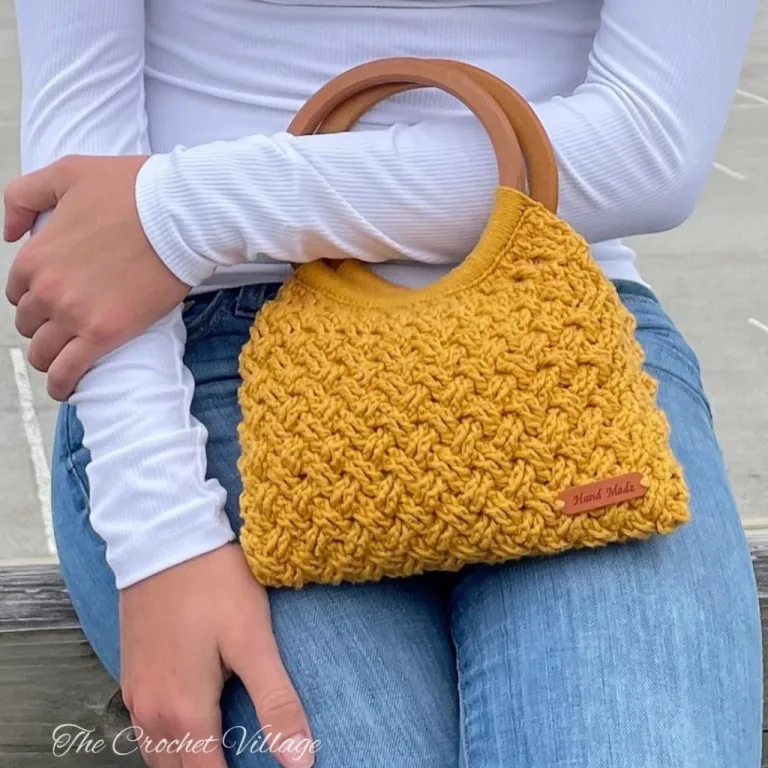 Woman holding a handmade crochet handbag with round wooden handles, showing the textured Celtic weave stitch detail