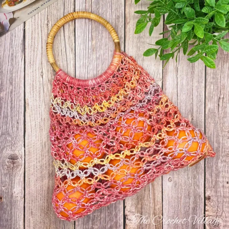 A crochet market bag with wooden handles, filled with fresh oranges.