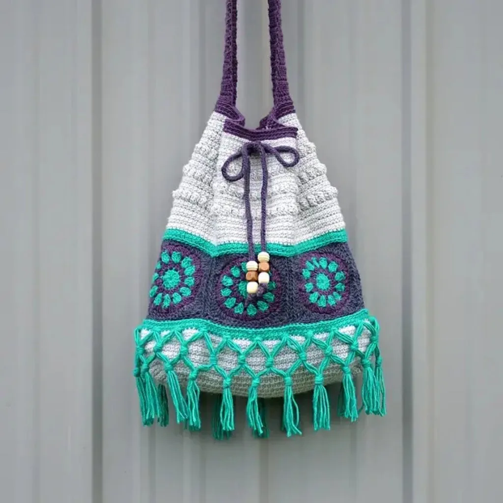 A crocheted boho crossbody bag featuring fringes and a string closure adorned with beads.