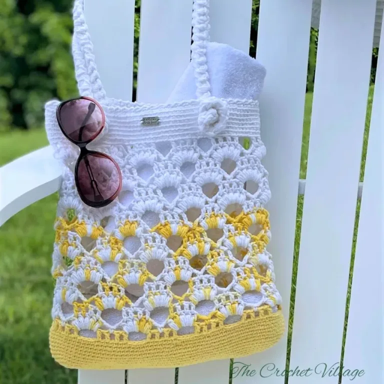 A crochet beach bag holding a towel and sunglasses hanging on a beach chair.