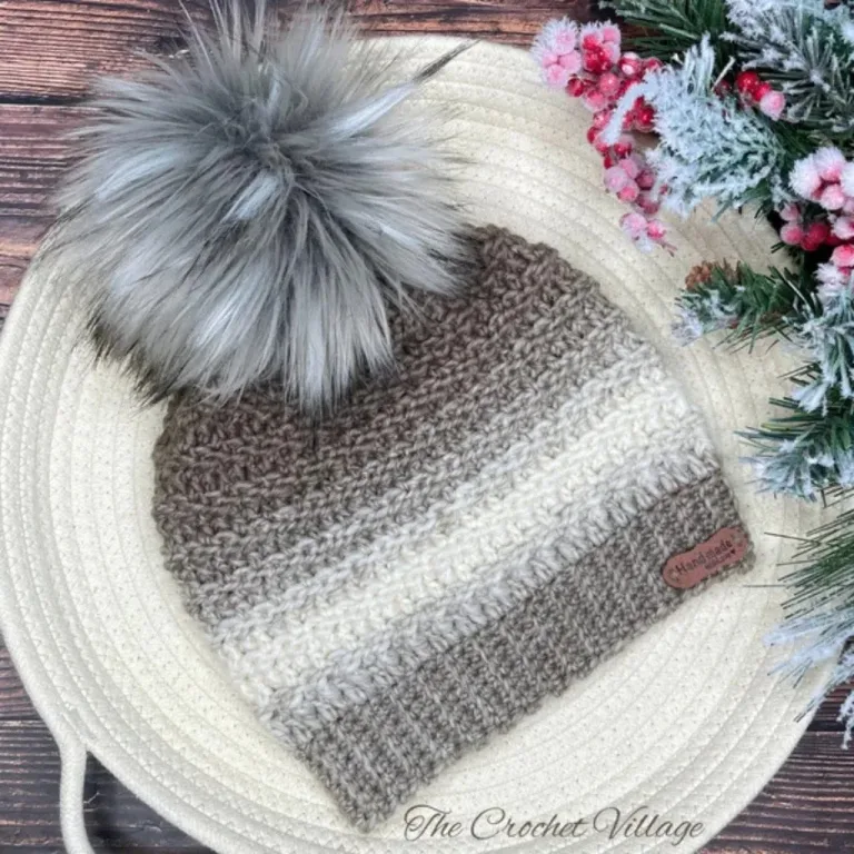 A crochet unisex, textured hat featuring a large pom pom, perfect for staying warm and stylish during the holiday season.