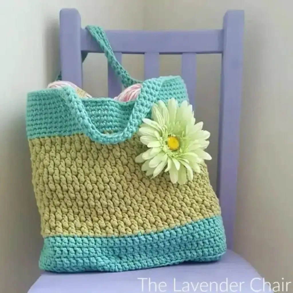 A lovely crochet chunky purse with a large flower, resting on a chair.