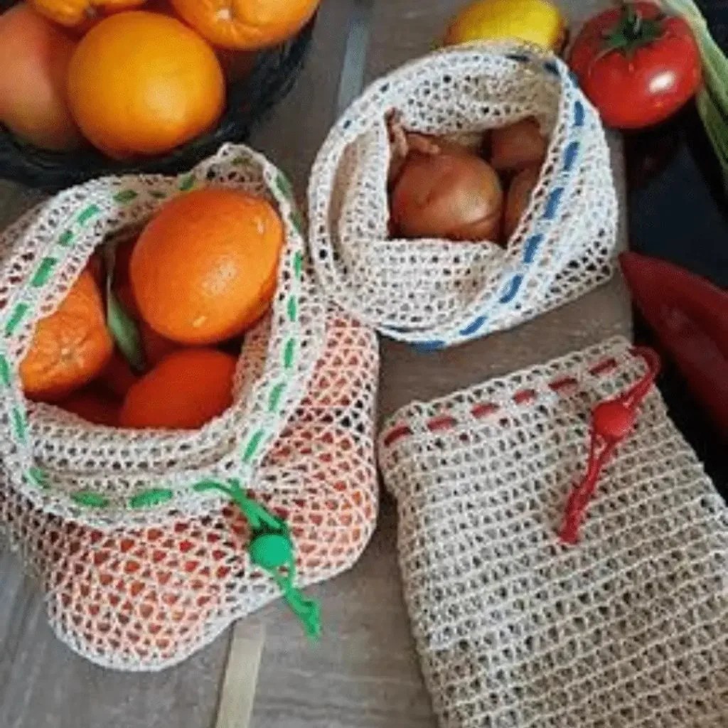 Three reusable crochet produce bags in different sizes, each filled with fruit.