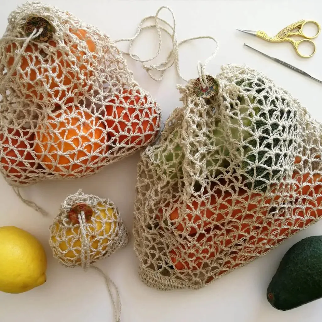 Three crochet V-stitch produce pouches in different sizes, each filled with fruit.